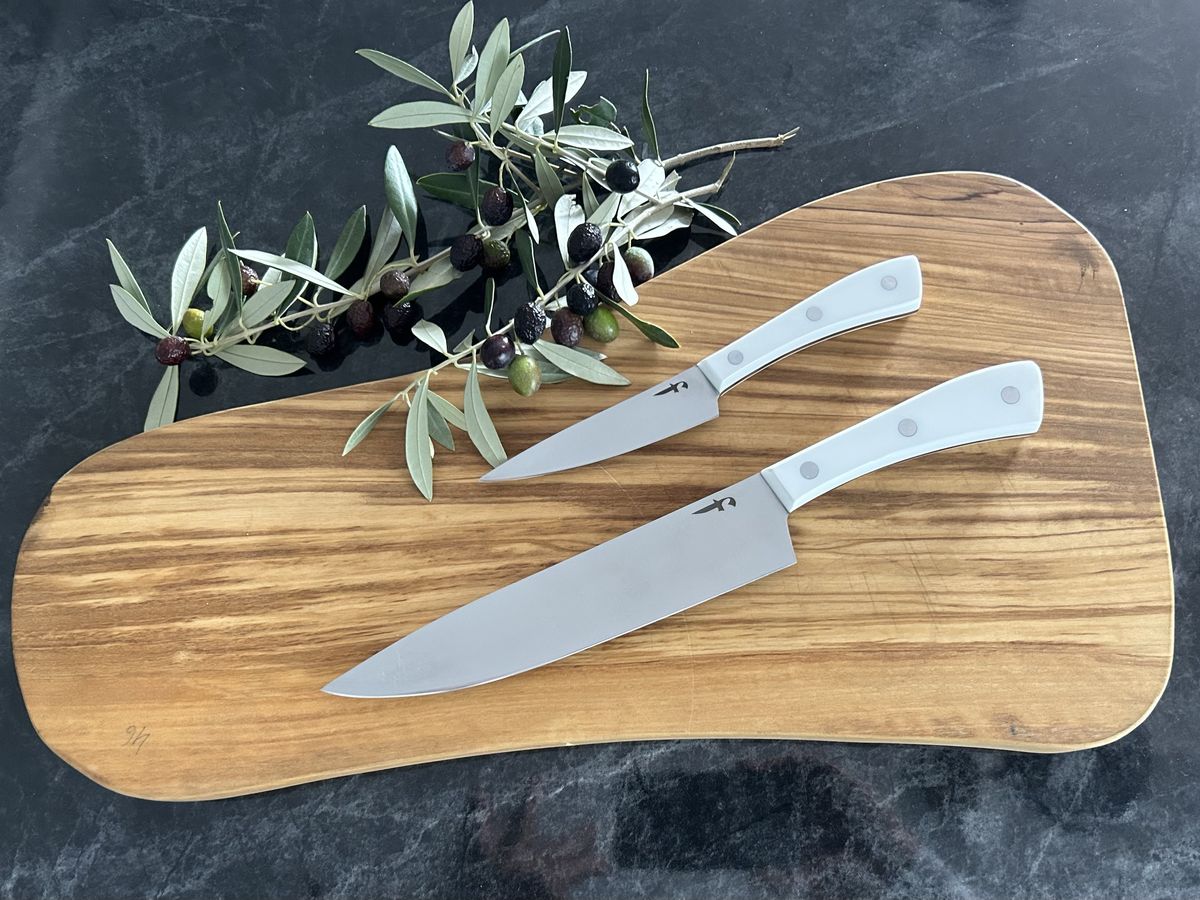 Dos cuchillos de cocina con mango blanco sobre una tabla de olivo